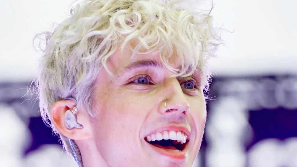 Troye Sivan smiling on stage under purple lights