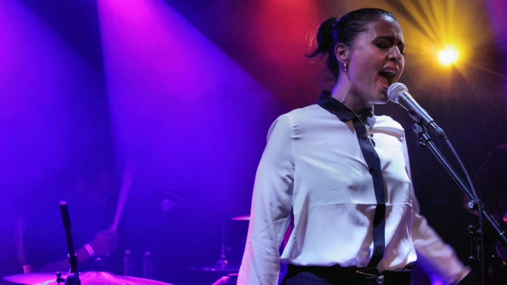 Jessie Ware singing at the microphone under purple stage lights