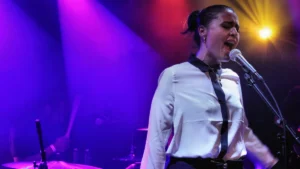 Jessie Ware singing at the microphone under purple stage lights