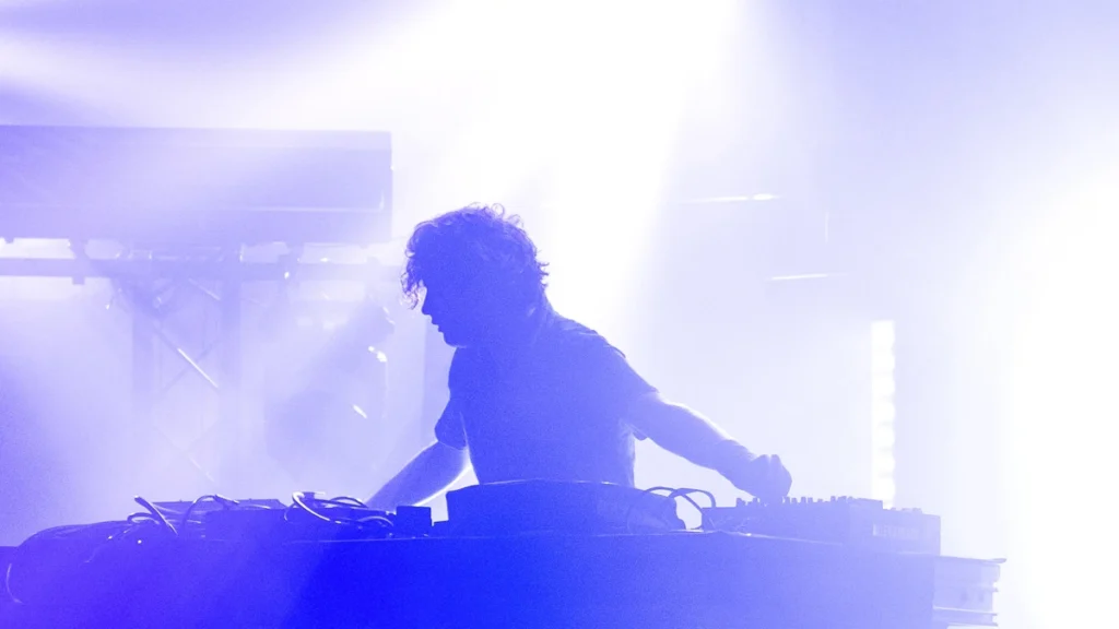 Nathan Fake performing live behind his hardware under stage lighting