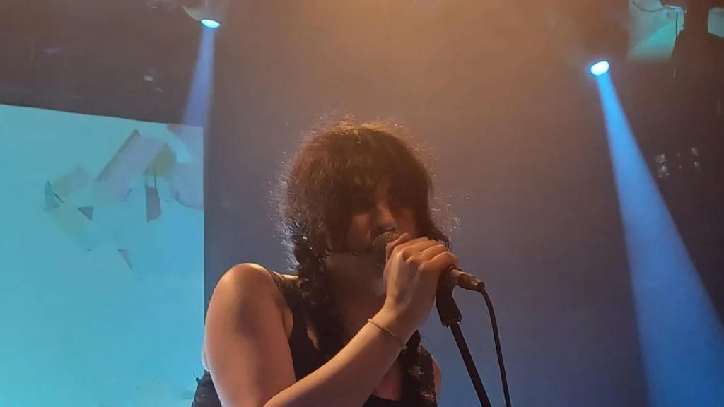 Underscores singing into a microphone under stage lights