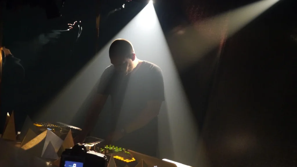 Com Truise performing over hardware in a beam of stage light