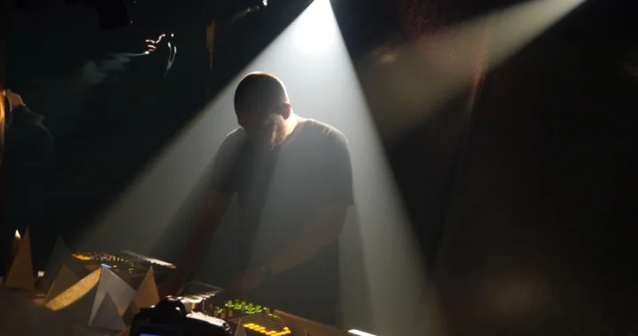 Com Truise performing over hardware in a beam of stage light
