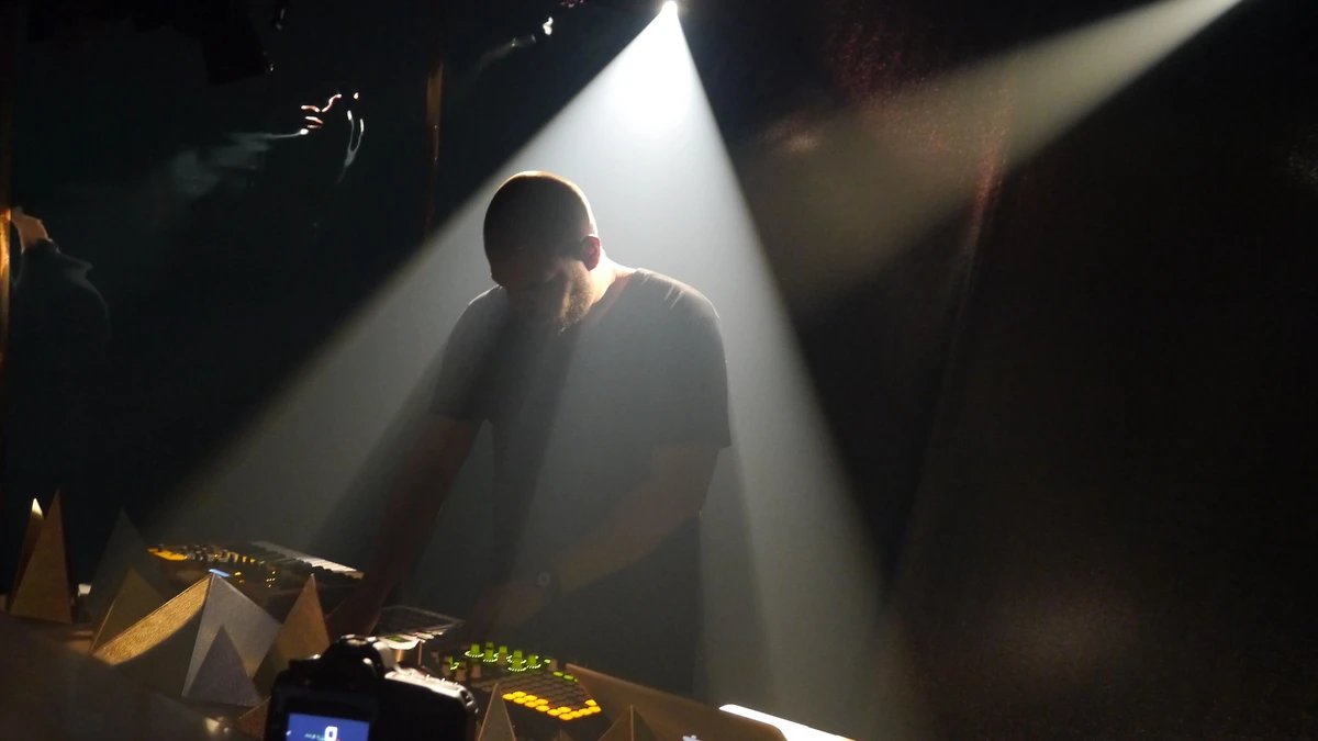 Com Truise performing over hardware in a beam of stage light