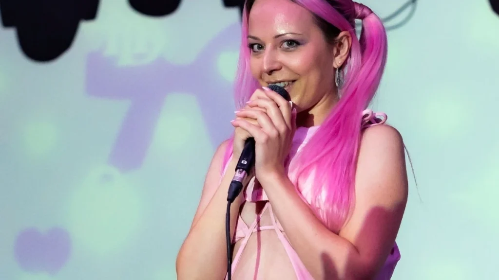 Hannah Diamond singing with pink hair against a pastel projection