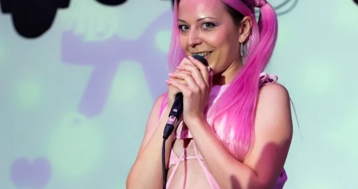 Hannah Diamond singing with pink hair against a pastel projection