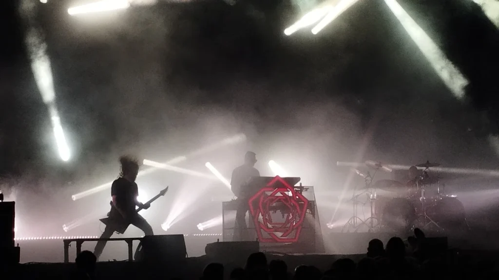 Carpenter Brut performing live with guitarist and drummer under beam lighting